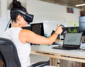 Une étudiante en design avec un casque de réalité virtuelle devant un ordinateur