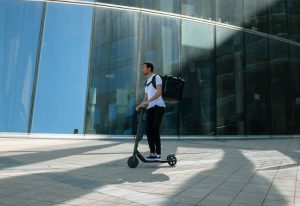 un jeune en t-shirt blanc roulant sur une trottinette électrique entre les immeubles d'une ville