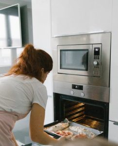 un four à pizza dans une cuisine avec une femme entrain d'enfourner une pizza
