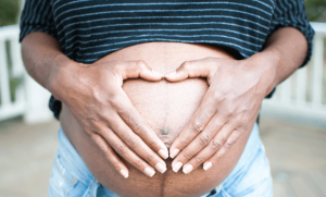 un ventre de femme enceinte avec un les main posée dessus formant un coeur