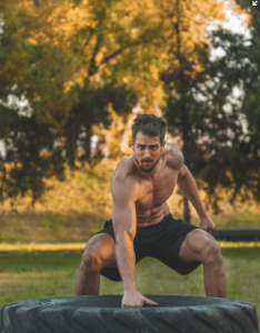 Un homme torse nu entrain de faire un Street Workout avec un pneu dans un parc